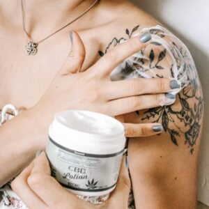 Tattooed woman applying CBD lotion on shoulder for skincare and relaxation.